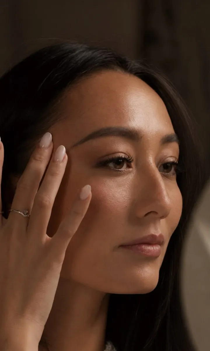 Femme aux cheveux bruns effleurant son sourcil, regard sublimé par une extension de cils, Maison GOĒN Paris 8e